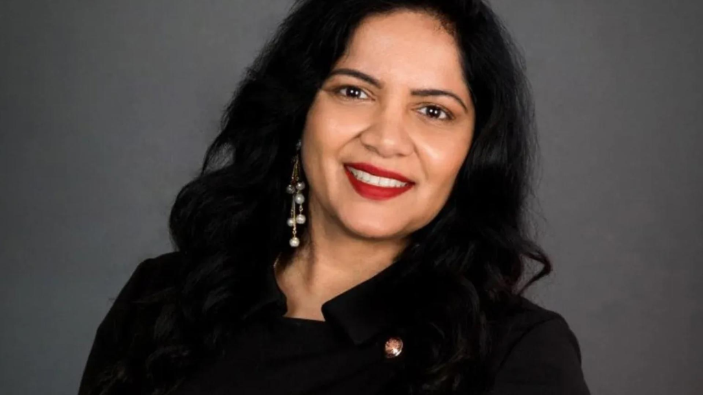 Woman with dark hair and red lipstick smiles at camera with gray background.