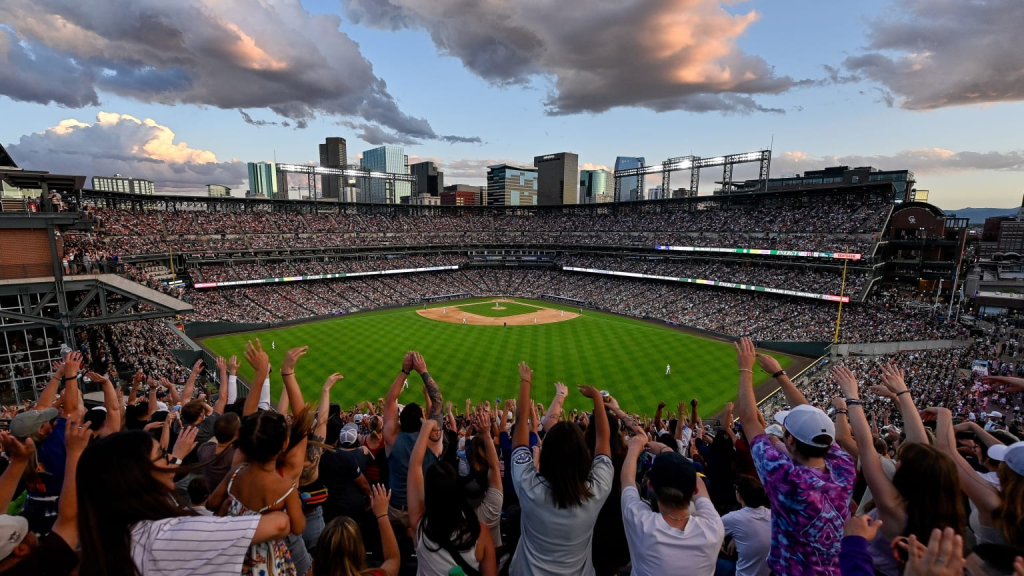 Fans with hands raised at Rockies game, city of denver in background