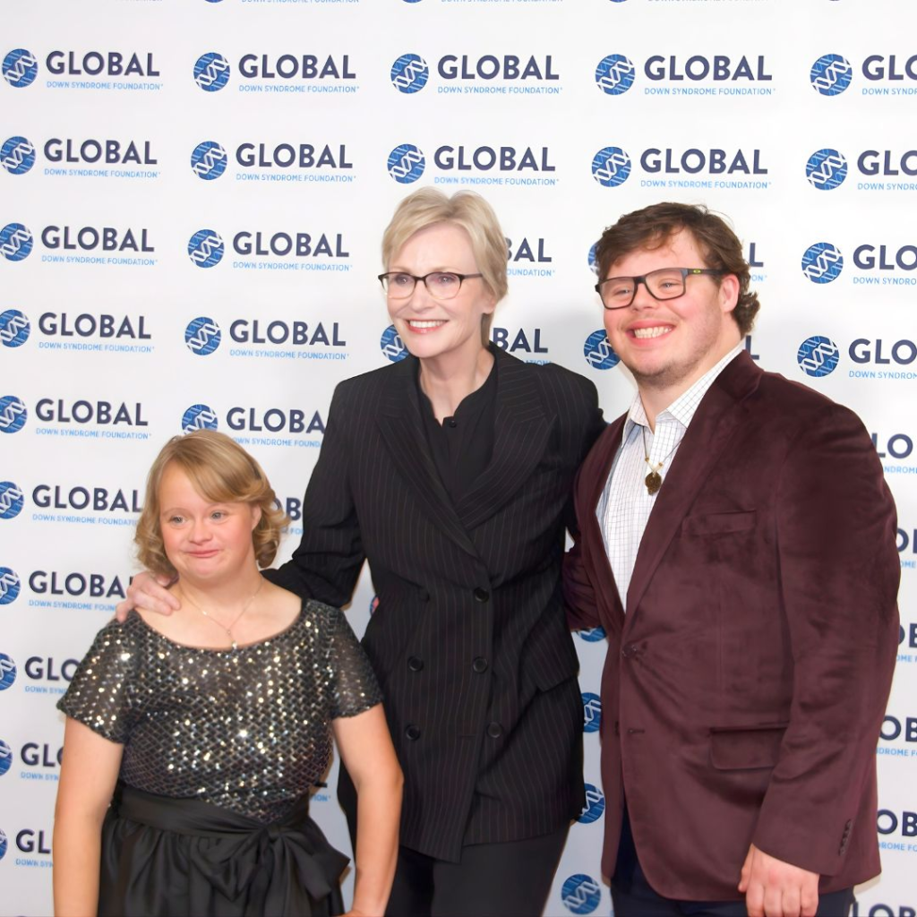 Actress Jane Lynch (blonde hair and black framed glasses, wearing a black suit in center), with Down syndrome advocate Lauren Potter (left - blond hair with sparkling black to hand black skirt) and actor James Day Keith (right - brown suit with white shirt and black framed glasses, brown hair)
