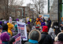A speaker addresses a crowd through a megaphone while protesters hold signs calling for ICE out of Colorado during a labor- and community-led rally outside Palantir Technologies in Denver.