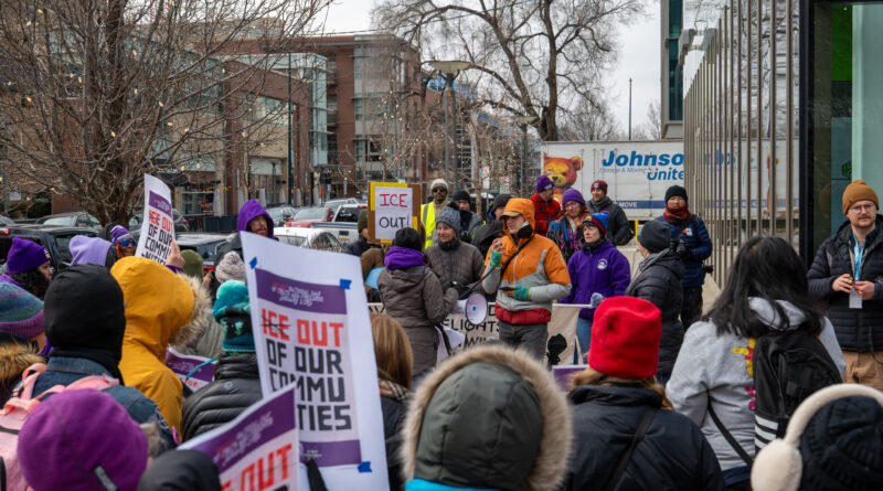 A speaker addresses a crowd through a megaphone while protesters hold signs calling for ICE out of Colorado during a labor- and community-led rally outside Palantir Technologies in Denver.
