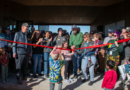 Lead donor David Smith, Executive Director Rachel Hutchens and camper Lily Prutch cut a bright red ribbon at the entrance of Bluff Lake Nature Center during the Feb. 14, 2026 grand opening celebration, surrounded by staff, families and community members applauding inside the new net-zero facility lobby.