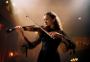 Young woman in black dress playing violin in a dark, moody setting.