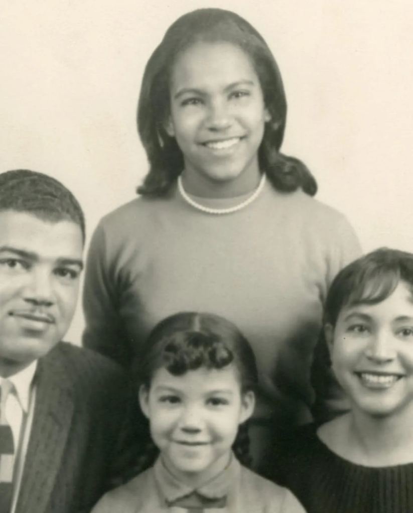 Black-and-white portrait of a family of four, with two adults and two children smiling and posed closely together.