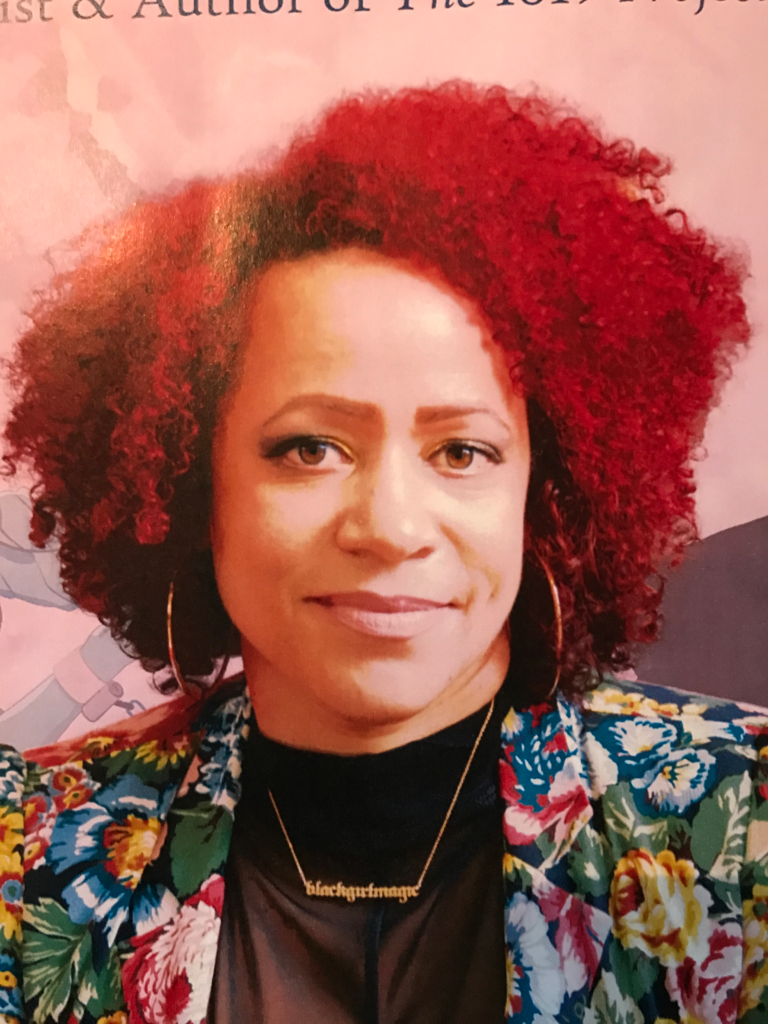 Close-up portrait of Nikole Hannah-Jones with curly red hair, wearing a floral jacket and a necklace that reads “blackgirlmagic.”
