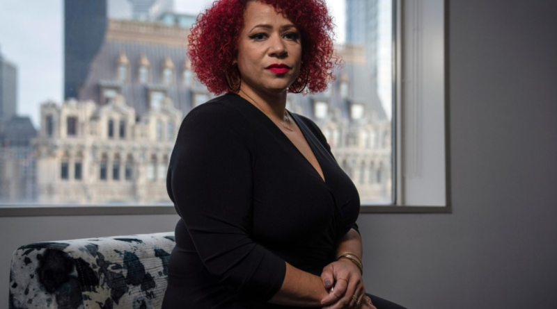 Nikole Hannah-Jones sits indoors in front of a window with a cityscape in the background, wearing a black dress and looking directly at the camera.