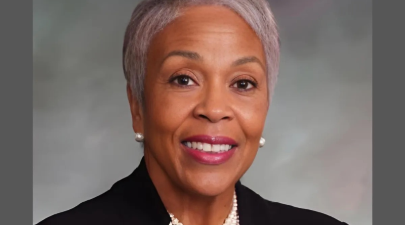 Professional portrait of Janet Buckner smiling, wearing a black blazer and pearl necklace against a neutral background.
