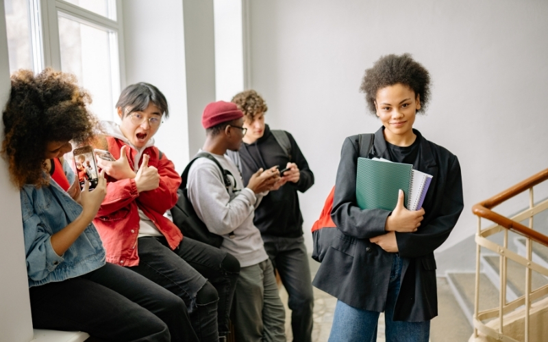 Diverse group of students gathered in a school hallway, with one student smiling while holding notebooks.