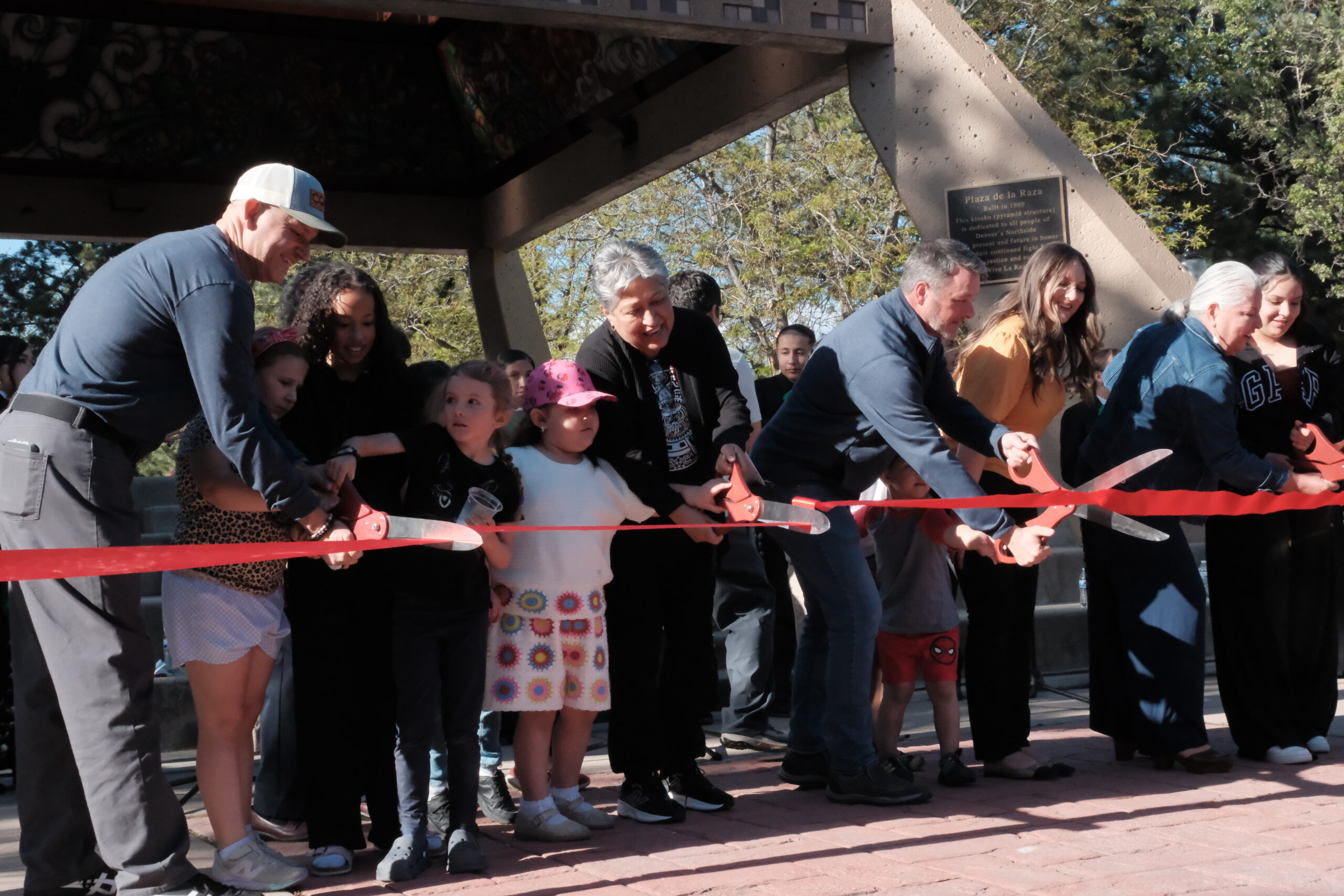 Community members, including children and local leaders, cut a red ribbon during the reopening ceremony at La Raza Park.