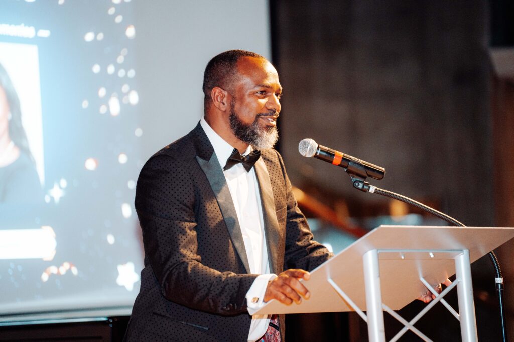 Dr. Fernando Branch delivers remarks from a podium during a Colorado Men of Color Collaborative event, speaking about leadership, community and impact.