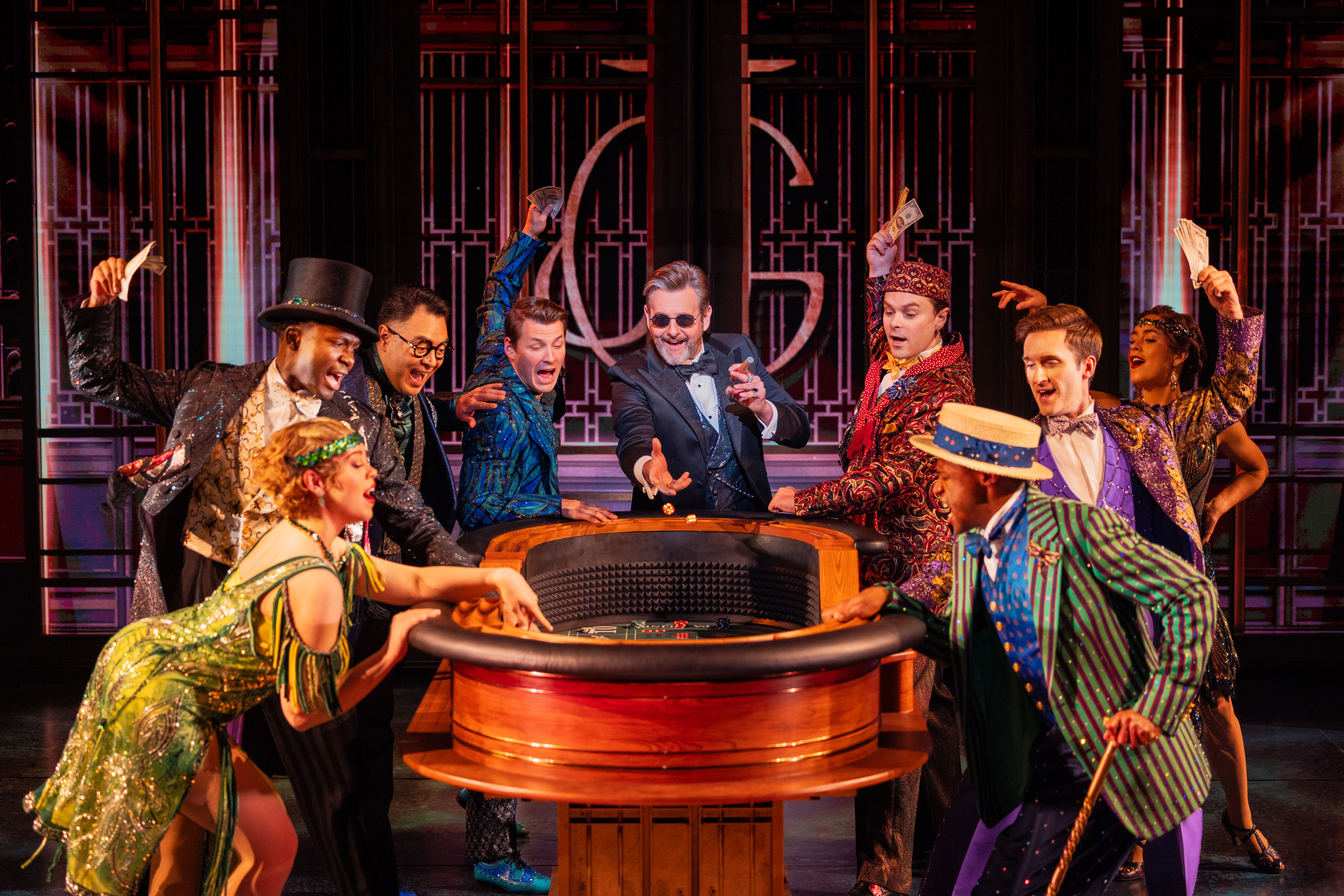 Cast members in glittering 1920s-inspired costumes gather around a roulette table during The Great Gatsby musical.