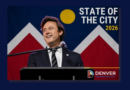 Denver Mayor Mike Johnston smiles while delivering the 2026 State of the City address from a podium, with the Denver city flag displayed behind him and the words "2026 State of the City" featured prominently on the graphic.