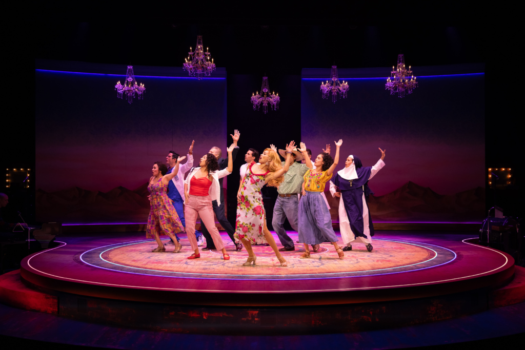 The cast of Destiny of Desire performs together on a circular stage beneath chandeliers and vibrant purple and pink lighting.
