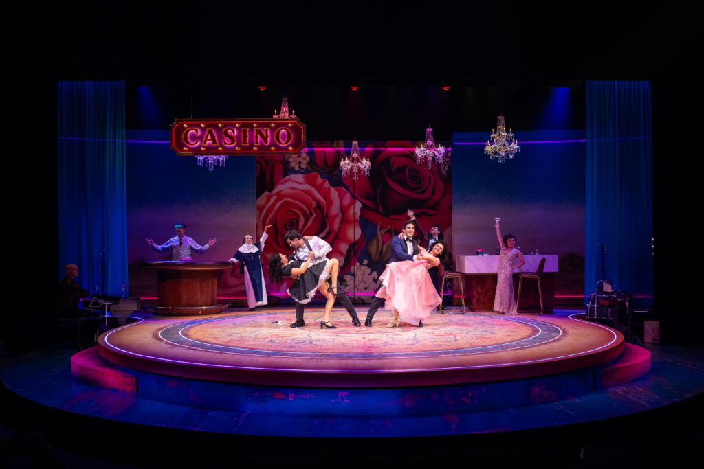 The cast of Destiny of Desire performs an energetic casino scene against a rose-covered backdrop with dramatic lighting and chandeliers.