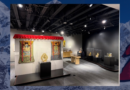 Interior view of the Heritage in Motion exhibition at the Museum of Boulder, layered over a Himalayan mountain landscape with the Nepalese flag in the foreground.