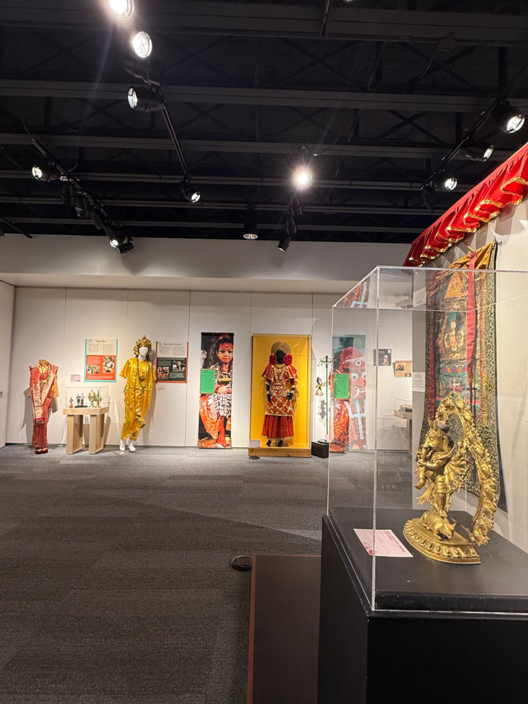 Interior of the Heritage in Motion exhibition featuring traditional Nepali clothing, religious and cultural objects, photography and artwork displayed throughout the Museum of Boulder gallery.
