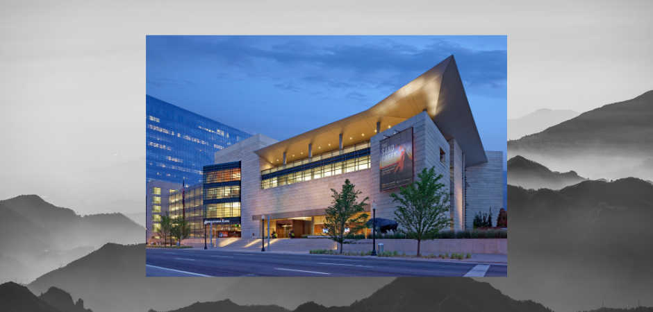 Exterior of the History Colorado Center in downtown Denver at dusk, featuring modern architecture, illuminated windows and a distinctive angular roofline.