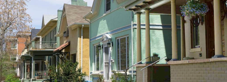 Colorful historic homes with front porches line a residential street in Denver, illustrating the established neighborhoods surrounding the proposed Burnham Yard redevelopment.